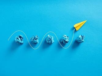yellow paper plane passes through crumpled blue paper balls